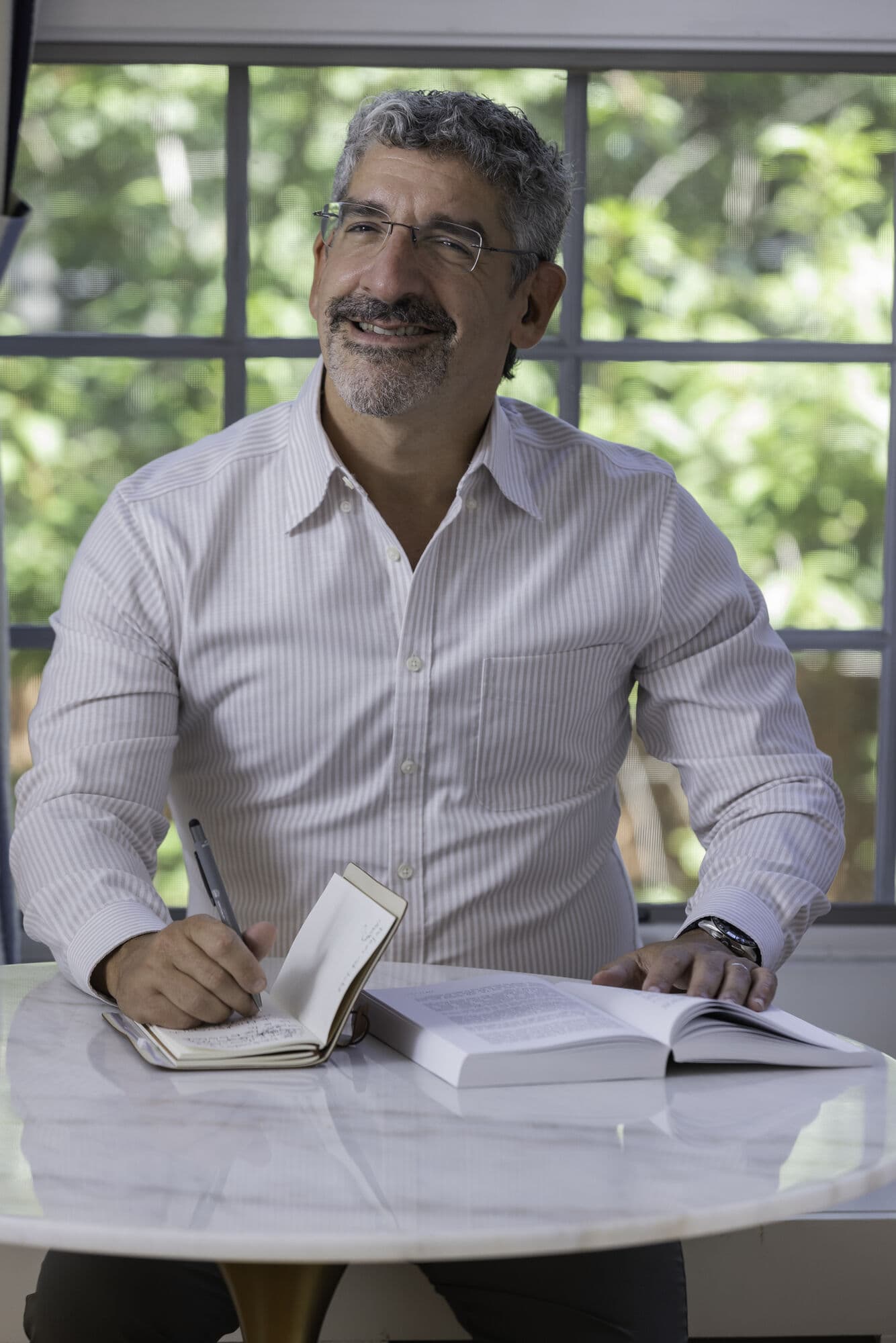 Dr. Jason Meisel at his desk by a sunlit window, pen in hand